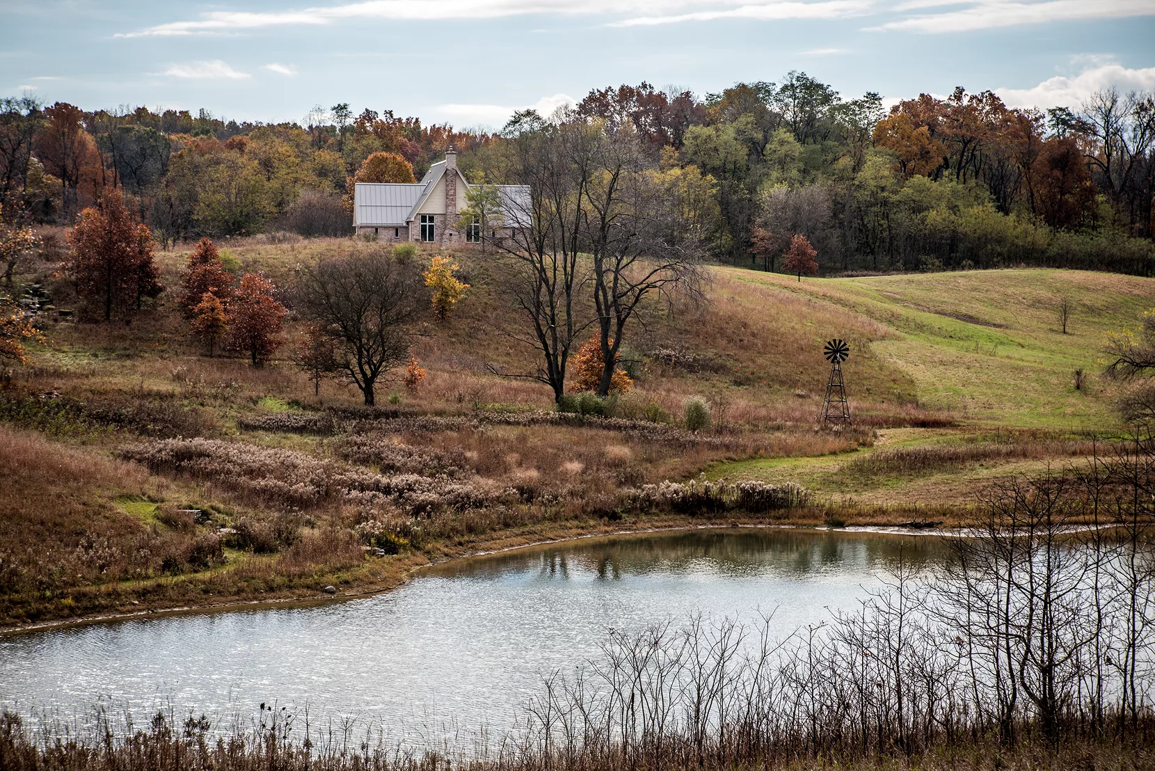 landscape of hills in fall with pond in foreground and brick building in background