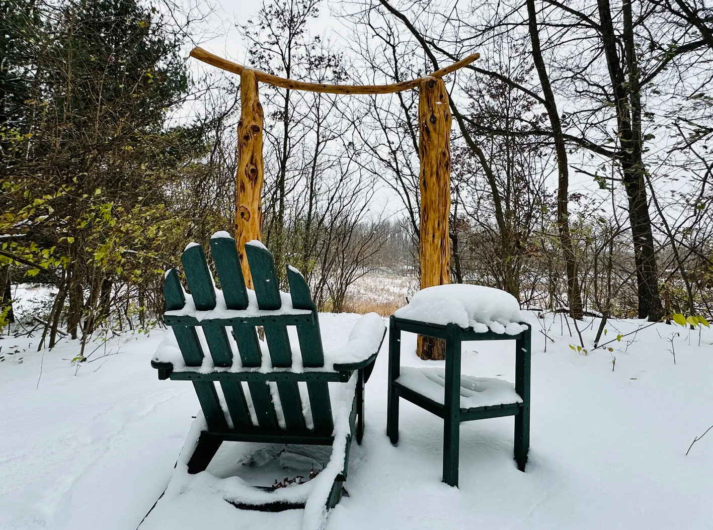Adirondack chair and table covered in snow with wooden arch