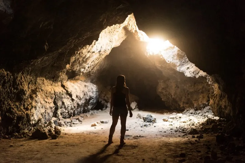 a person stand in a shadowy cave, facing the light coming from above