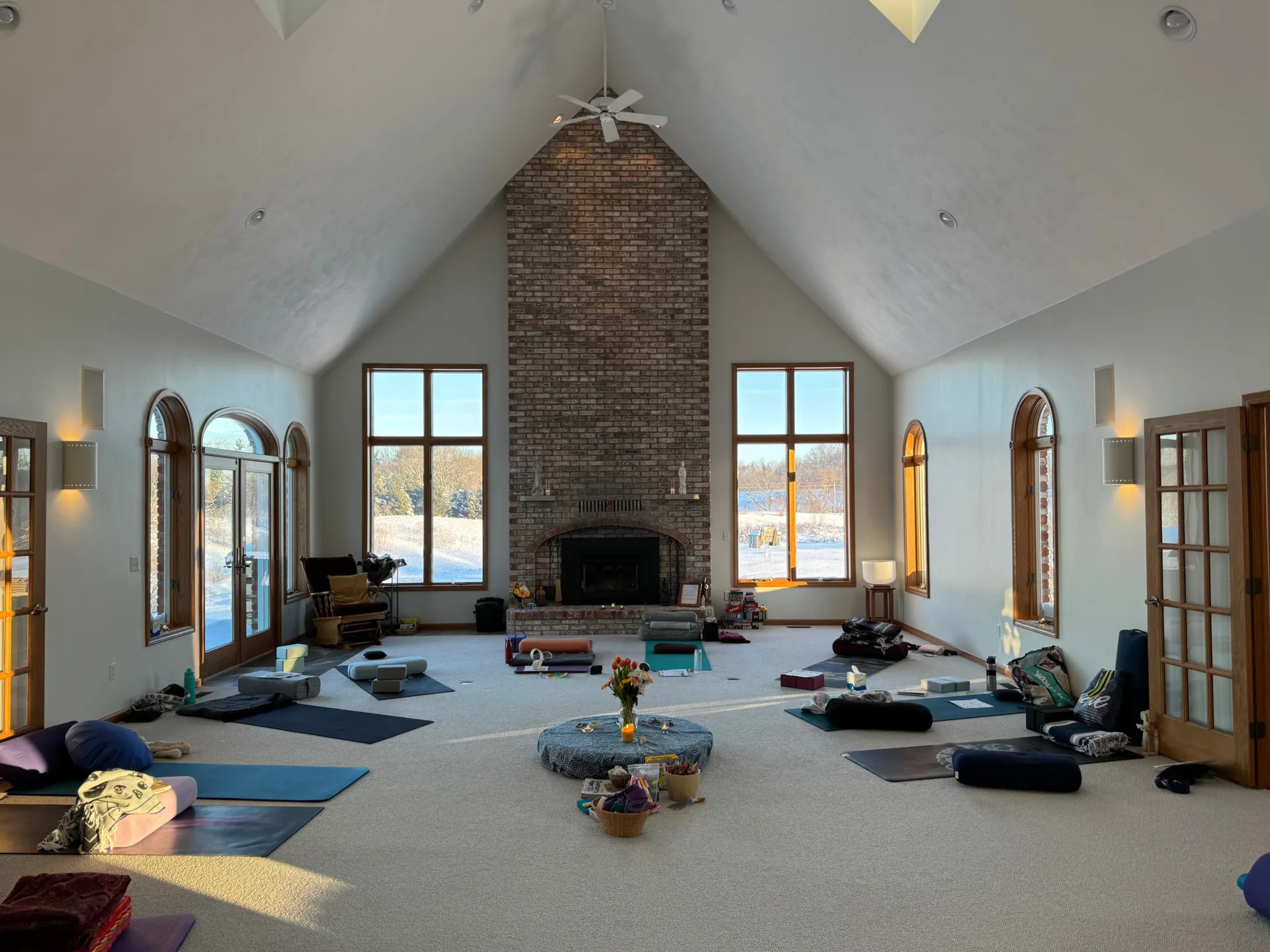 A large white room with tall ceiling, filled with yoga mats and yoga supplies