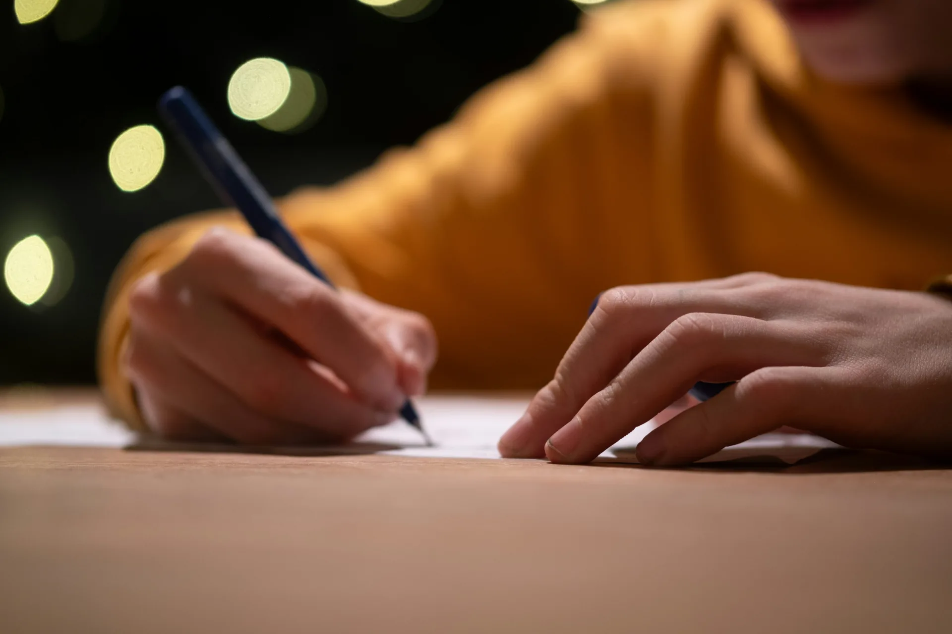 person wearing orange shirt writing on paper with soft lights in the background