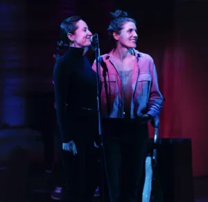 Two women standing at a microphone and smiling