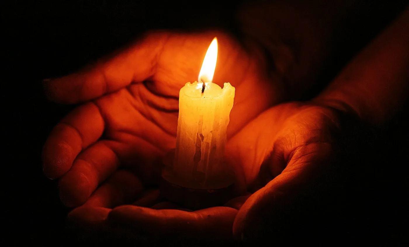 Two hands holding a candle, glowing in the darkness